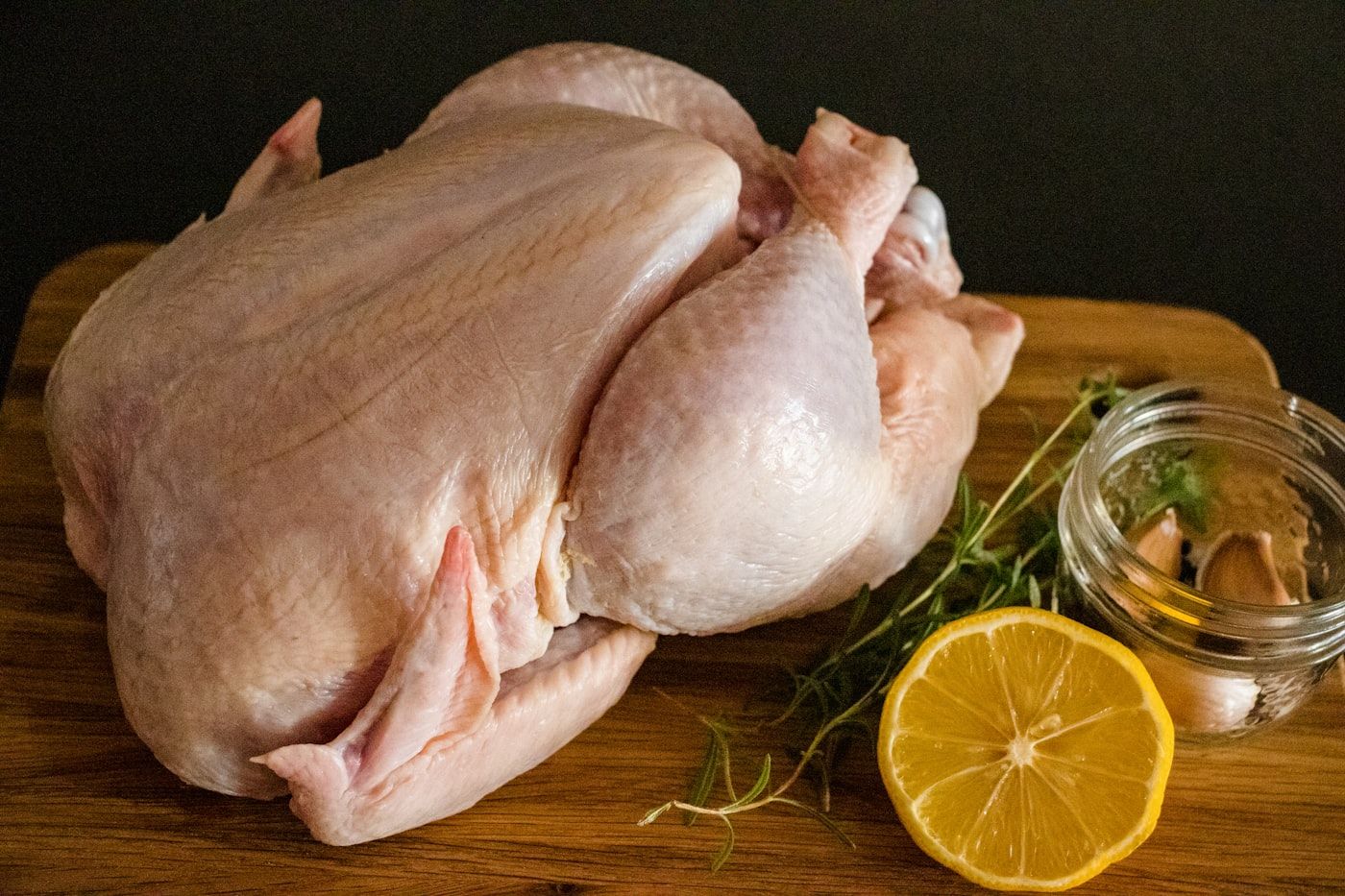 A whole fresh raw chicken on a wooden board with a lemon half